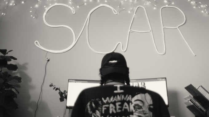 A person looking at a computer screen with SCAR in lights above their head.